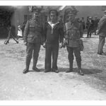 3rd DCLI recruiting march, The Lizard, Landewednack, Cornwall. 29th June 1915. Lance Corporal Thomas Rendle VC is standing on the left and Coast Guard Edwards is in the centre. Lance Corporal Rendle was born in Bedminster, Bristol, on the 14th December 1884. At the time of his award he was a bandsman in the 1st Battalion, Duke of Cornwall's Light Infantry and was acting as a stretcher bearer. He was 29 years old. His citation reads "For his conspicuous bravery on 20 November 1914 near Wulvergem, when he attended to the wounded under very heavy shell fire and rifle fire, and rescued men from the trenches in which they had been buried by the blowing in of the parapets by the fire of the enemy's heavy howitzers". He was the only stretcher bearer to receive a Victoria Cross in World War 1. His medal is held at the DCLI museum in Bodmin. He was awarded the medal by King George V on 12 July 1915. He died in 1946 in Cape Town South Africa. Coast Guard Edwards is wearing naval uniform. The Coast Guard (later known as Coastguard) was part of the Admiralty between 1856 and 1923. Photographer: Arthur William Jordan..