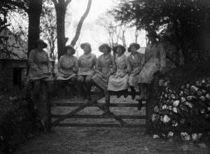 Seven members of the Women's Land Army sitting on a gate at Tregavethan Farm, facing towards the camera. The names of the women are as follows, left to right: Ms Trejeweth, unknown, Ms Brown, Ms I Crowther, Mrs Ford, Md Dorothy Phyllis Martin, unknown. The women’s uniform consists of boots, gaiters, felt hats and pale fabric overalls. Photographer: A W Jordan. © From the collection of the RIC (TRURI-1972-2-82).